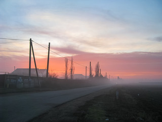Fototapeta na wymiar Dawn Foggy Morning Behind a Village Outskirts and an Asphalt Road