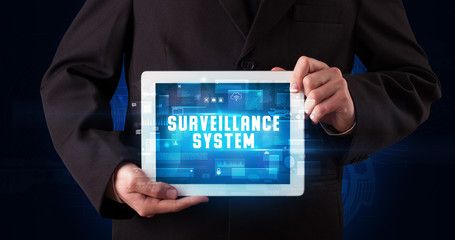 Young business person working on tablet and shows the digital sign: SURVEILLANCE SYSTEM