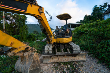 The modern excavator on the construction site with sunset sky. Large tracked excavator standing on a hill with a green grass. Machinery for a construction of a new building in the countryside.