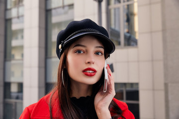 Cryptic charming lady with red lips in kepi talks on cellphone and looks at you enigmatically
