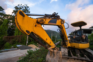 The modern excavator on the construction site with sunset sky. Large tracked excavator standing on a hill with a green grass. Machinery for a construction of a new building in the countryside.