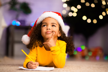 Wistful little afro girl thinking about letter to Santa Claus