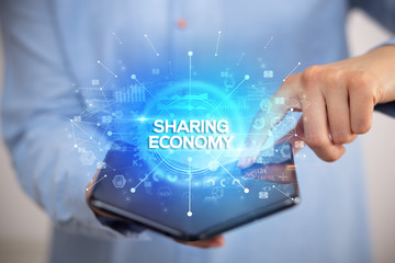 Businessman holding a foldable smartphone with SHARING ECONOMY inscription, new business concept