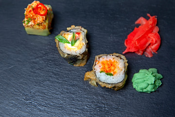 Three Sushi Roll with shrimps, tobiko caviar, wasabi, pickled ginger on black slate board