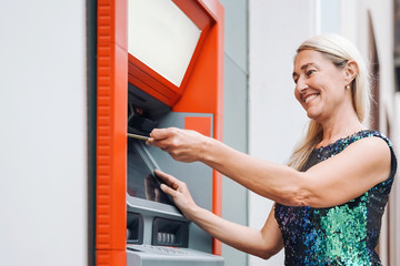 Happy mature woman withdraw money from bank cash machine with debit card - Senior female doing payment with credit card in ATM - Concept of business, banking account and lifestyle people
