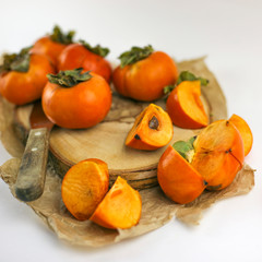 Persimmon lies on a wooden Board on a white background. Persimmon close - up whole and cut into slices with a knife. Organic farming, healthy food concept, eco-friendly products, vegetarian, raw 