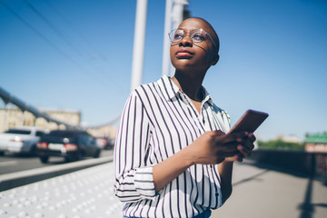 Thoughtful woman with mobile phone sitting on city bridge