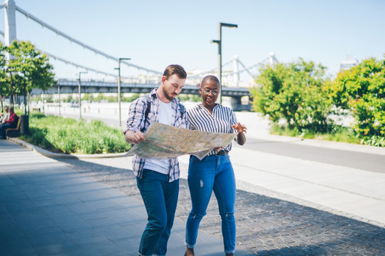 Multiracial couple of travelers using map in street