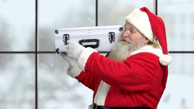 Senior Santa holding case with dollars. Christmas Santa Claus with cash money on checkered window background. Christmas bonuses to employees.