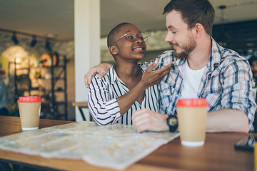 Lovely multiracial couple hugging and enjoying meeting at table in cafe