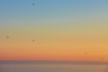 Silhouette of powered paraglider soaring flight over the sea against marvellous orange sunset sky.