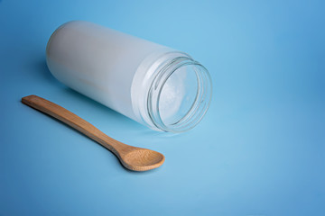 Coconut oil cosmetics for skin and hair care. Oil in cream jar, bamboo spoon on light blue background. Top view. Flat lay.