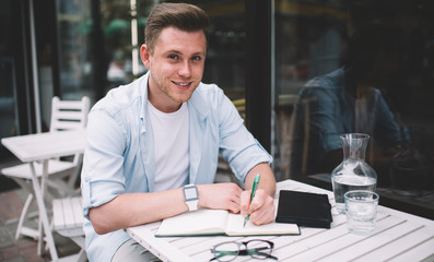 Fototapeta premium Cheerful guy making notes in outdoor terrace
