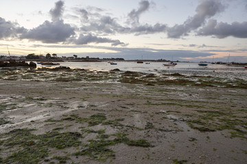 Beach in Brittany with low tide, small boats in the shallow water, houses in the background, dramatic sky