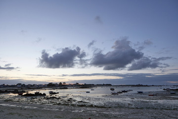 Beach in Brittany with low tide, small boats in the shallow water, houses in the background, sky with clouds, silence