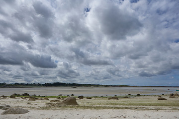 Bay in Brittany at low tide, with small rocks, trees in the background, cloudy sky, silence