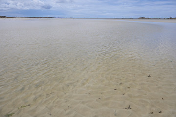 Ebb at a beach at the coastline of Brittany, blue sky, summer