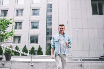 Cheerful man drinking coffee walking in urban street