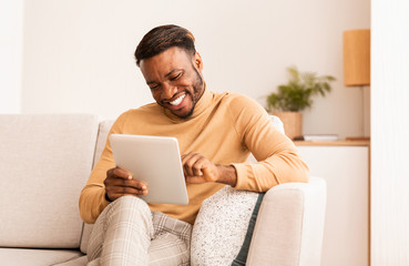 Black Guy Using Tablet Smiling Sitting On Sofa At Home