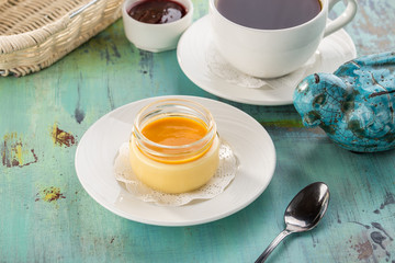 Fruit dessert panna cotta with mango in glass jar and cup of black tea on blue wooden table
