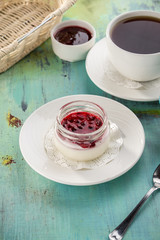 Dessert panna cotta with cherry jam and cup of black tea on blue wooden table