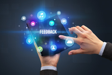 Businessman holding a foldable smartphone with FEEDBACK inscription, social media concept