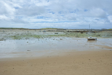 Fototapeta na wymiar Coast in Brittany at low tide with sand and seaweed and small boats, cloudy blue sky, silent mood