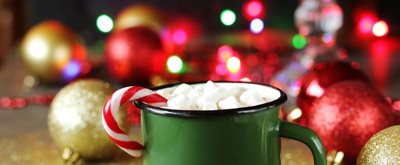 hot cocoa or chocolate with marshmallows and Christmas candy in an enameled mug against the background of festive lights and bokeh. place for text. copy space