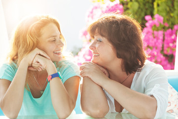 Happy beautiful young mother and adult daughter chatting laughing in the sunlight, happiness family...