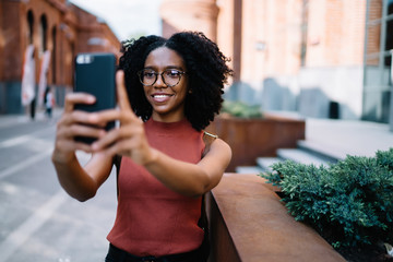 Optimistic African American tourist taking selfie exploring city