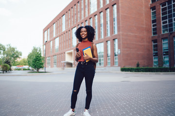 Naklejka premium Smiling black lady with cellphone and books in hand