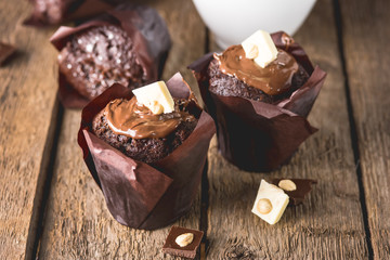 Three Tasty Chocolate Muffins Decorated with Chocolate on Wooden Background White Cup of Cococa with Dark Photo Vertical