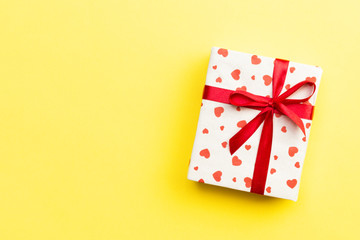 Gift box with red ribbon and heart on yellow background, top view with copy space for text