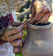 A craftsman creates a ceramic product on a pottery wheel. Hands are covered with raw clay.
