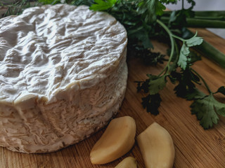 Camembert cheese with garlic and herbs on wooden board
