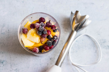 Frozen berries, cut apples, bananas and other fruits in plastic blender glass or flask. Ready to make pulp or smoothie. Vegan or vegetarian food concept. Morning time light.