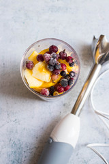 Frozen berries, cut apples, bananas and other fruits in plastic blender glass or flask. Ready to make pulp or smoothie. Vegan or vegetarian food concept. Morning time light.