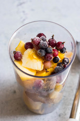 Frozen berries, cut apples, bananas and other fruits in plastic blender glass or flask. Ready to make pulp or smoothie. Vegan or vegetarian food concept. Morning time light.