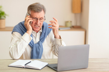 Discontented Senior Man Talking On Phone Sitting In Modern Office