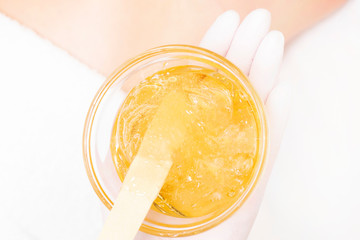 Depilation concept. close up a cup with shugaring paste, on a blurry background you can see part of the client skin. white