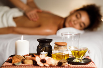 Fototapeta na wymiar Afro girl enjoying back massage with aroma candle and oils