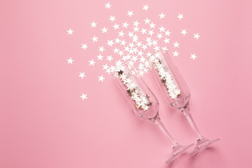 Champagne glasses with silver stars confetti on pink color paper background minimal style