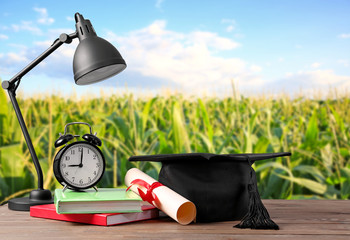 Mortar board, diploma, lamp, clock and books on table. Concept of high school graduation