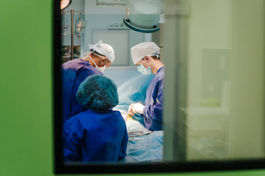 Surgeons in the operating room are pictured through the window. Selective focus