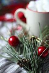 Bump in a pine branch with red Christmas toys on a background of a cup with marshmallows