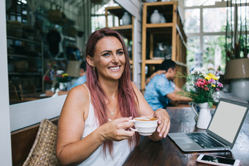 Pleased lady enjoying coffee near laptop