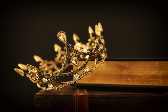 low key image of beautiful queen/king crown over old book and wooden table. vintage filtered. fantasy medieval period
