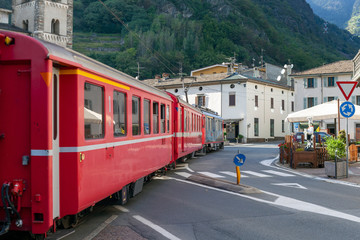 Red train on Tirano city street, Italy.