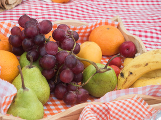 Several fruits on a red and white checked for a picnic