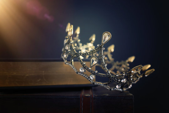 low key image of beautiful queen/king crown over old book and wooden table. vintage filtered. fantasy medieval period
